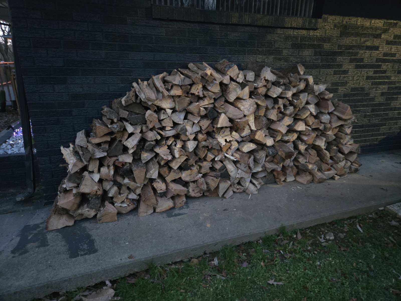 Split firewood stacked on a concrete slab beside a brick wall